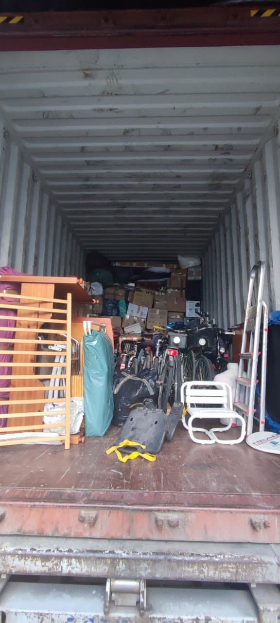 Intérieur du container rempli de meubles, vélos et cartons.