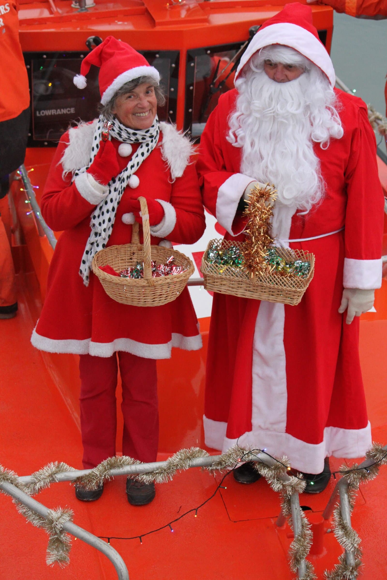 Père Noël et une bénévole costumée tenant des paniers de friandises au marché de Noël.
