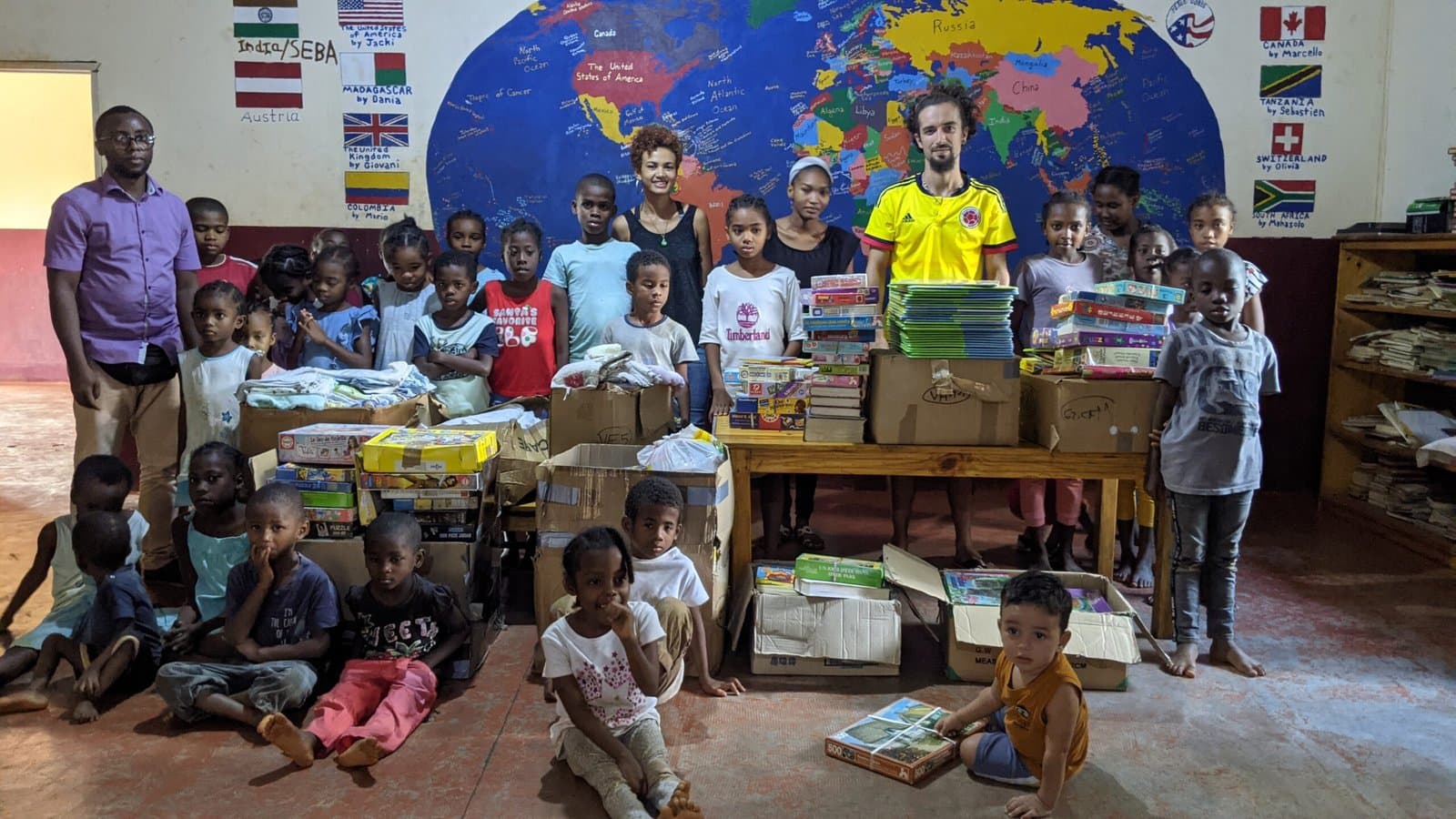 Bénévoles avec les enfants devant des cartons de fournitures scolaires reçues.