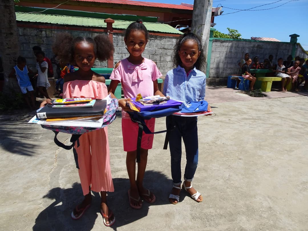 Trois fillettes tenant leurs cahiers et fournitures scolaires reçus en récompense.