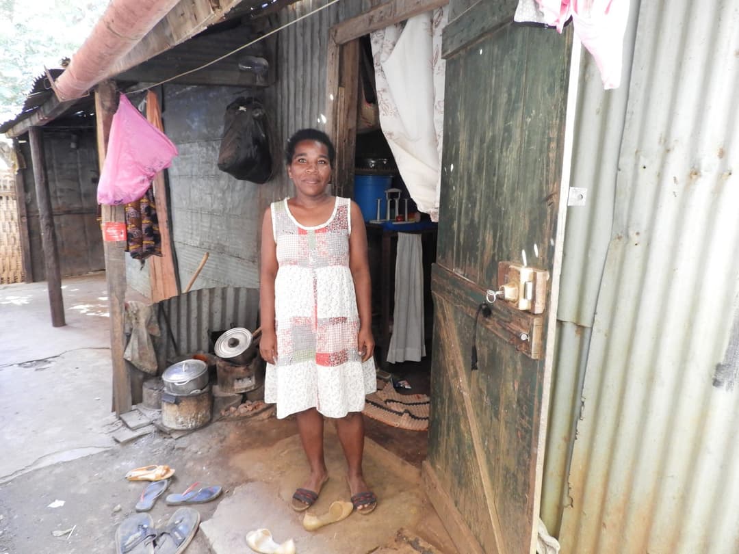 Femme debout dans l'encadrement de la porte de son habitation en tôle.