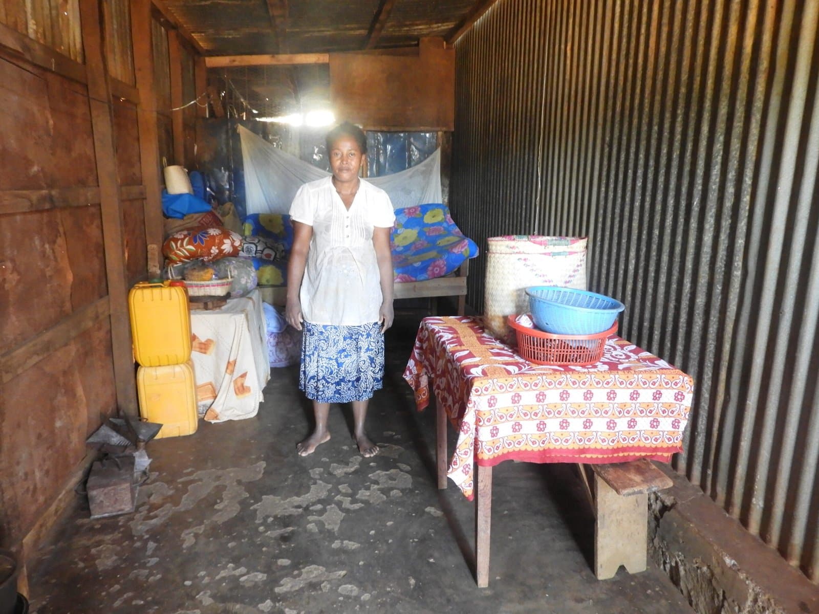 Femme debout dans son habitation, près d'une table dressée avec des bidons d'eau.