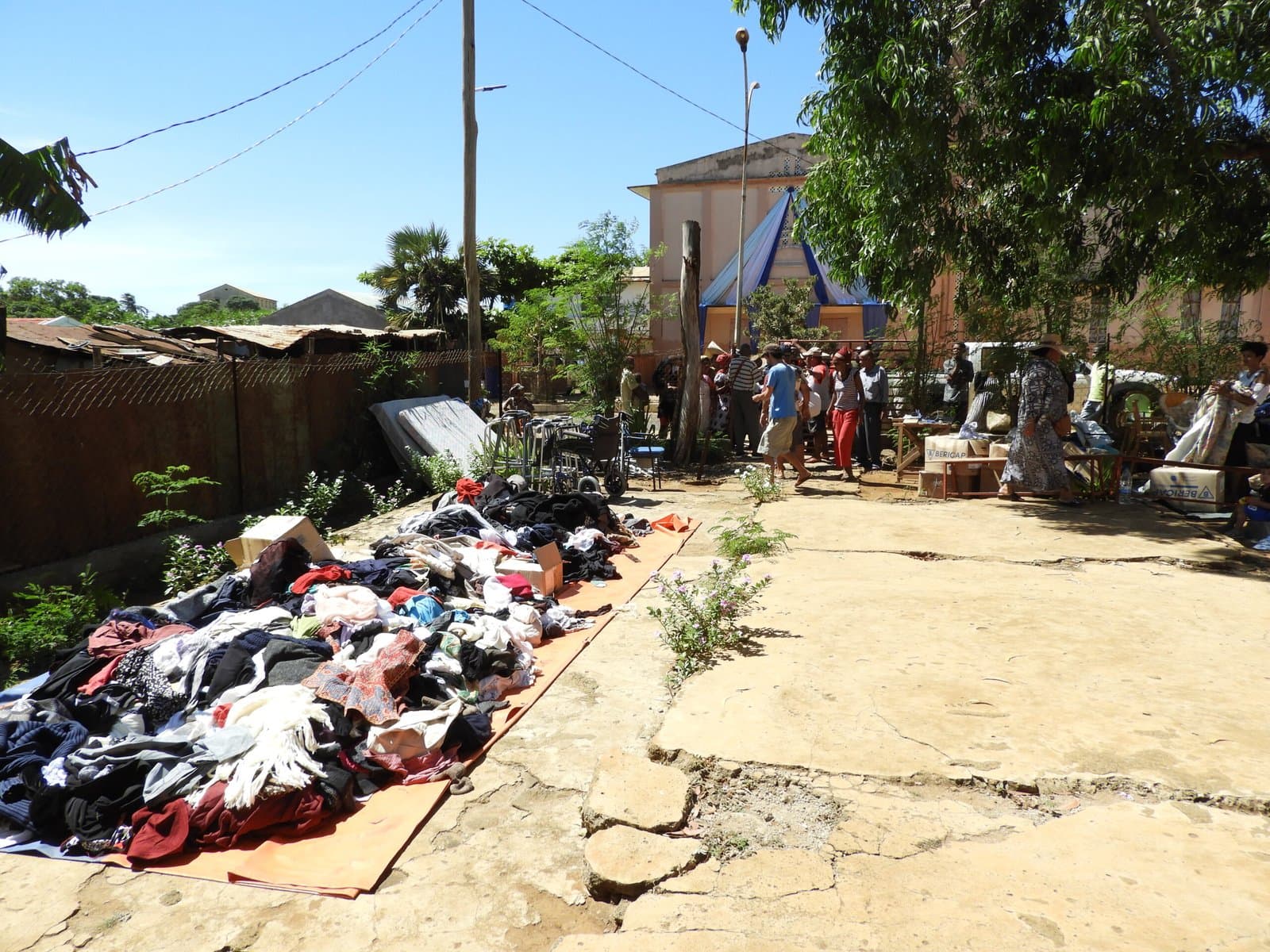 Vue d'ensemble du site de distribution, vêtements donnés étalés au sol et habitants rassemblés.