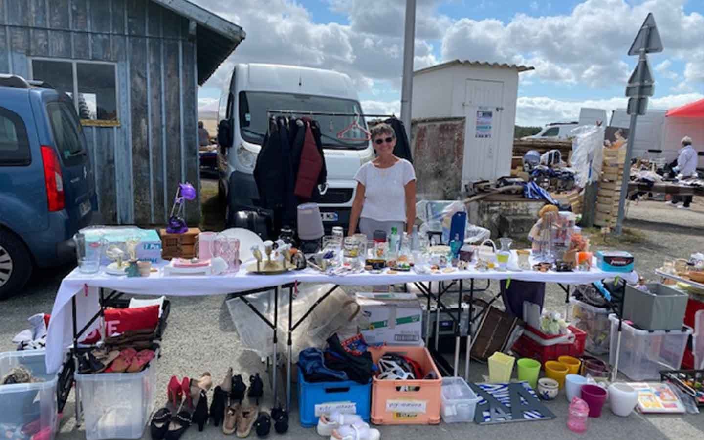Bénévole devant un stand de vide-grenier avec des objets à vendre.